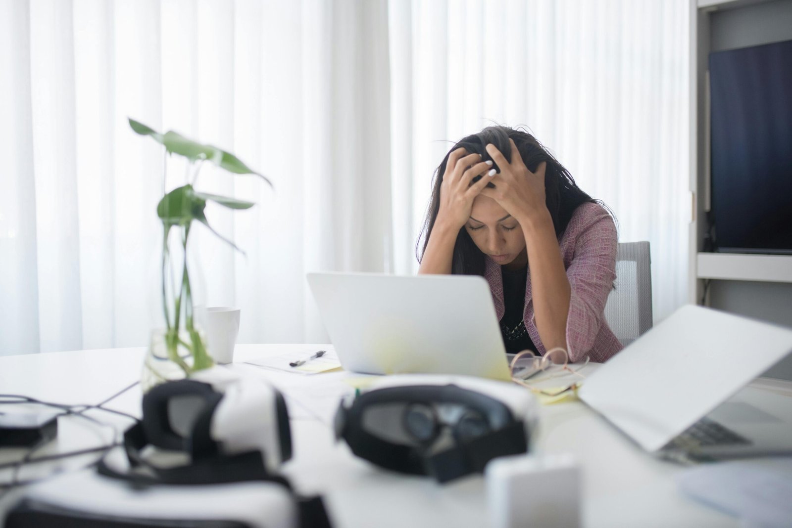A stressed woman holding her head while working on a laptop, showing daily mistakes that reduce productivity at work