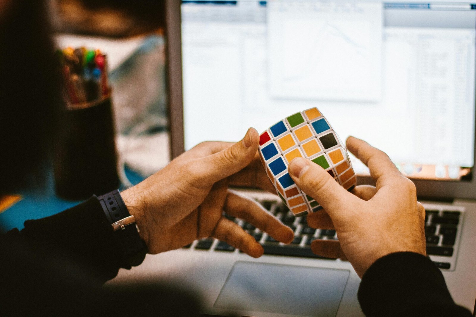 Person holding a colorful Rubik’s Cube while sitting in front of a laptop, showing distraction during work