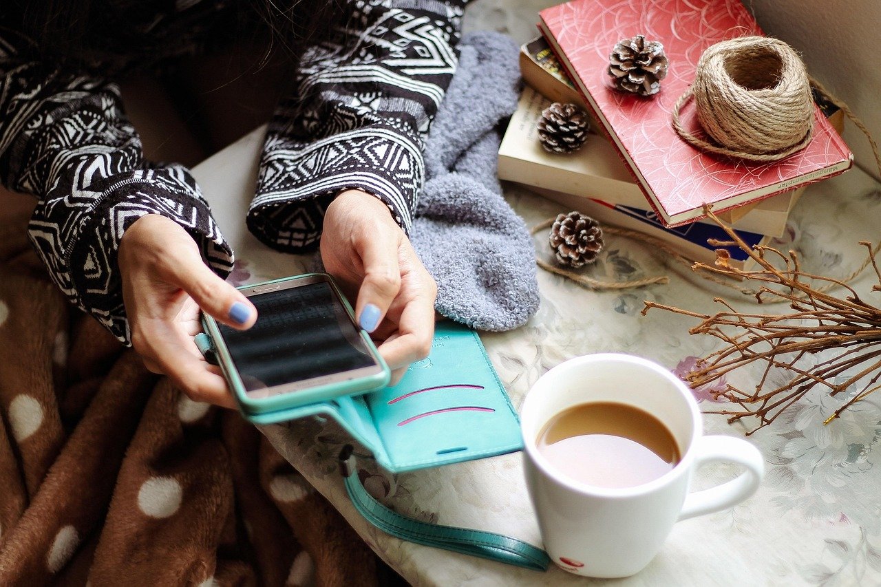 Person checking a smartphone while sitting at a table with a cup of coffee