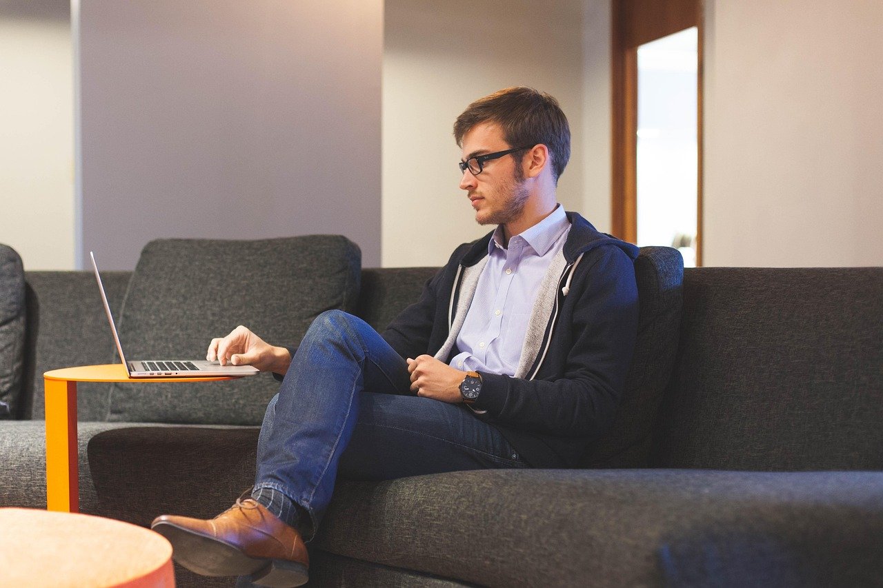Man sitting on a sofa using a laptop, feeling unmotivated and low on energy while working indoors
