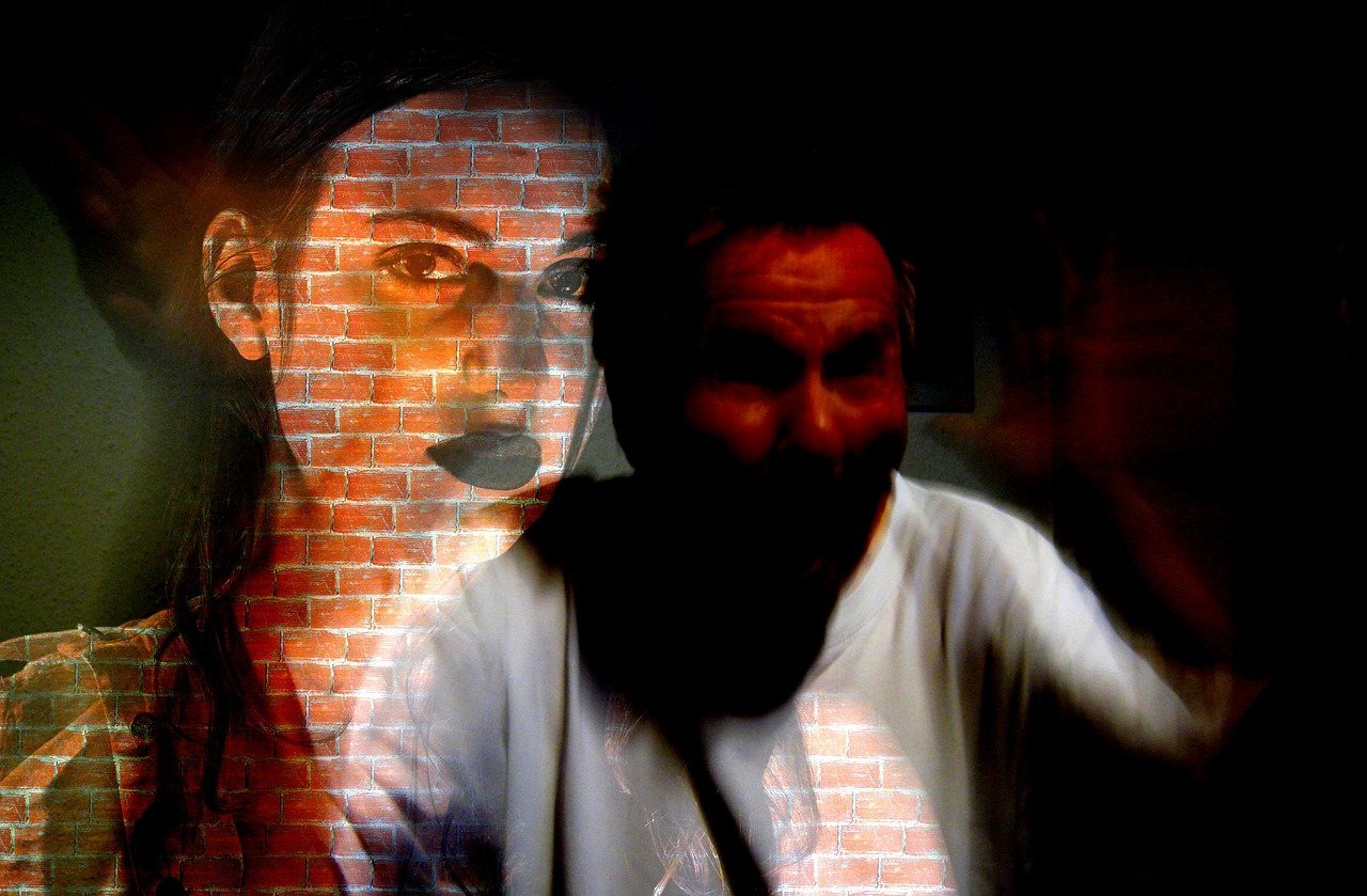 Double exposure image showing a woman’s face over a brick wall and a blurred figure in darkness, symbolizing difficulty focusing and mental distraction